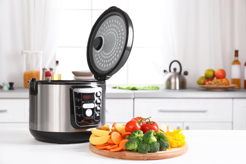 Modern multi-cooker with vegetables on wooden board